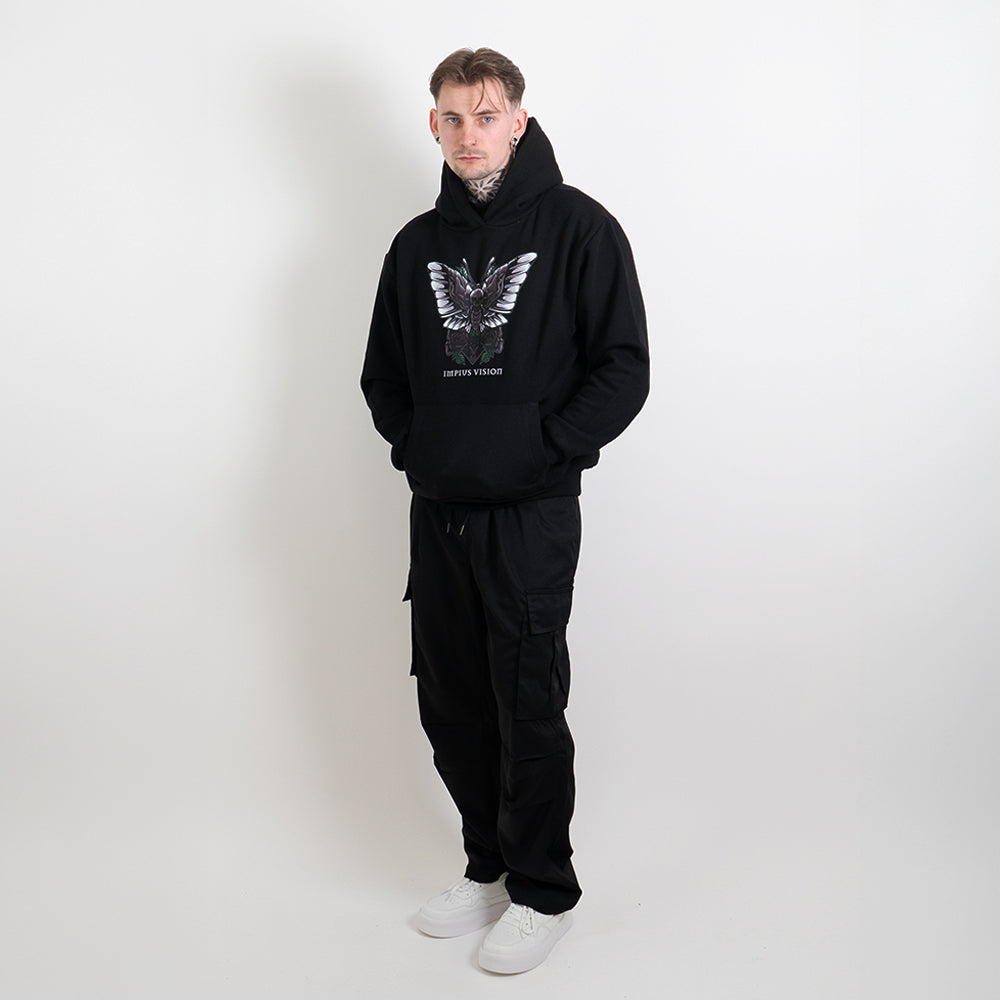 A fully body image of a tattoed model wearing a black hoodie with the impius death moth design